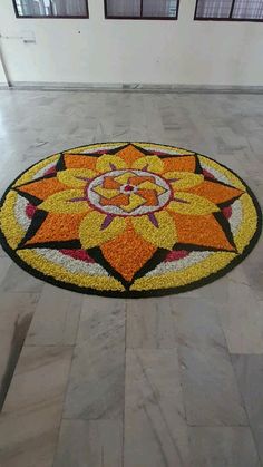 a circular rug with an orange and yellow flower on the floor in front of two windows