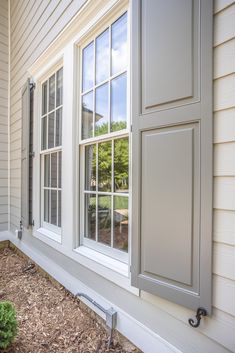 an open window on the side of a house with white siding and brown mulch