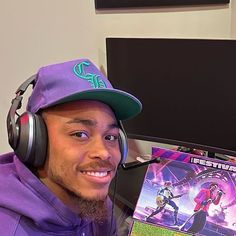 a man wearing headphones and a purple hoodie is holding up a video game