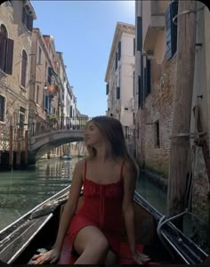 a woman in a red dress sitting on the back of a boat down a canal