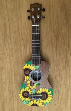 an ukulele with sunflowers painted on the front and back, sitting on a wooden surface