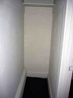 an empty narrow hallway with white walls and black flooring on the side walk way