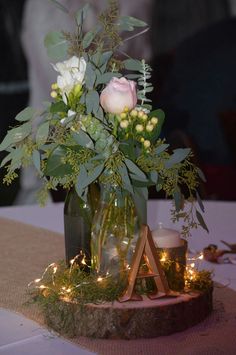 a vase filled with flowers and greenery on top of a wooden stand next to candles