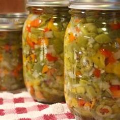 four jars filled with pickles and vegetables sitting on a checkered tableclothed cloth