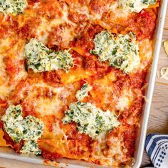 a casserole dish with spinach, cheese and sauce in it on a wooden table