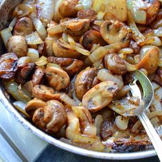 a pan filled with onions and mushrooms on top of a stove next to a spoon