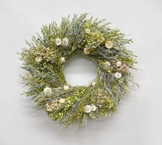 a wreath with white flowers and greenery hanging on a wall in front of a gray background