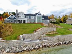 a large house sitting on top of a lush green hillside next to a lake with lots of trees