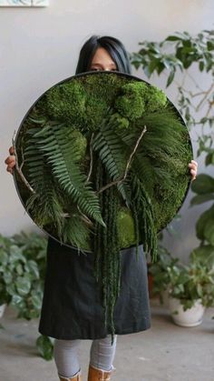 a woman holding up a large green plant in front of her face, with plants behind her