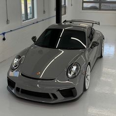 a grey sports car is parked in a large room with white walls and windows on the side