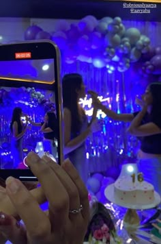 a woman taking a photo with her cell phone in front of balloons and streamers