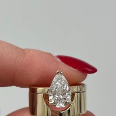 a woman's hand holding a yellow gold ring with a pear shaped diamond