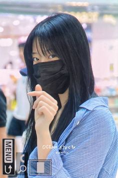 a woman with black hair wearing a mask and pointing to her finger at the camera