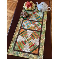 a table runner made out of quilts on top of a wooden table next to a tea pot