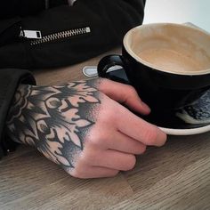 a person with tattoos on their arm holding a cup of coffee