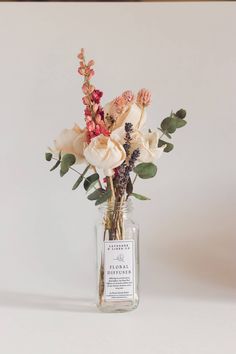 A Nustad Family Ranch Wild Magnolia Reed Diffuser with Pink Larkspur in a clear bottle with a white label, displaying an arrangement of pale roses, pink blooms, and eucalyptus leaves against a plain light background. Pink Larkspur, Family Ranch, Dried Florals, Traditional Candles, Home Spray, Reed Diffusers, French Lavender, Wood Flowers, Hand Body Lotion