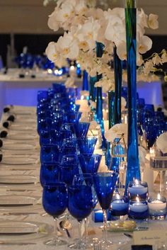 there are many blue vases and glasses on the table with white flowers in them