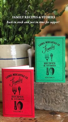 two cookbooks sitting on top of a table next to a pot filled with plants