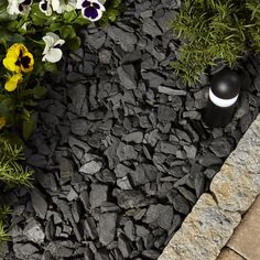 a black and white vase sitting on top of a rock garden path next to flowers