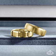 two gold wedding bands sitting next to each other on top of a gray surface with a window in the background