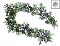 a wreath made out of green leaves and plaid ribbon on a white wall with the letter c