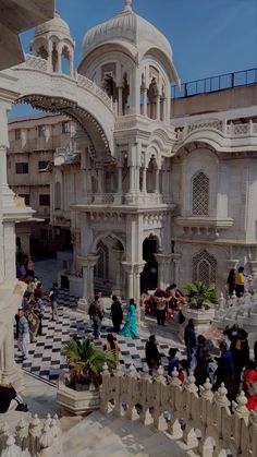 many people are walking around in front of a building with white pillars and arches on the sides