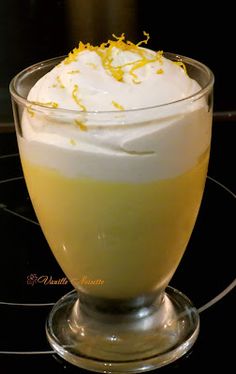 a glass filled with liquid and topped with whipped cream, lemon zest and garnish