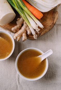 two cups of soup sit on a table with carrots and celery