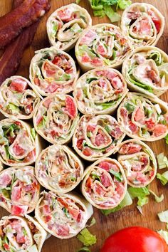 several wraps filled with meat and vegetables on top of a cutting board next to tomatoes