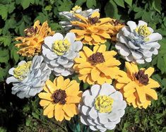 a vase filled with yellow and white flowers in front of green leaves on the ground