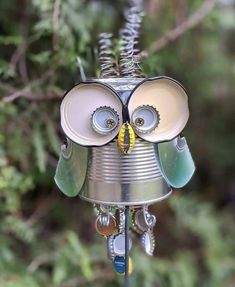 a tin can owl ornament hanging from a tree branch with its eyes open