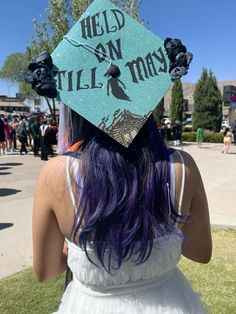 a woman with purple hair wearing a graduation cap that reads, help on till mass