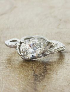 a white gold and diamond engagement ring on a wooden surface with the center stone partially covered in filigree leaves