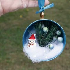 a person is holding a christmas ornament with balls and pine needles in it