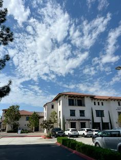 cars parked in front of an apartment building under a blue sky with white fluffy clouds