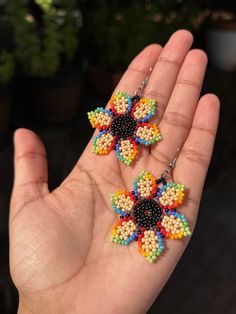 a person's hand holding two colorful beaded earrings