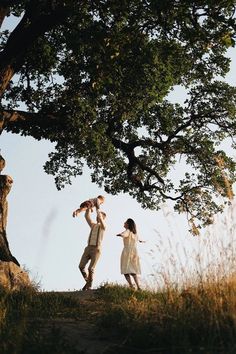 a man and woman standing under a tree with their arms around each other as they look at the sky