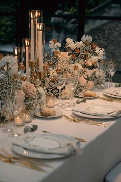 the table is set with white and gold place settings, silverware, candles, and flowers