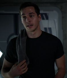 a young man in a black t - shirt is holding a gray towel and looking at the camera