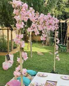 a table set up with pink flowers and place settings for an outdoor birthday party in the backyard