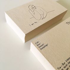 two business cards with drawings on them sitting on top of a white table next to each other