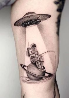 a woman's arm with an alien tattoo on it and a spaceship above her