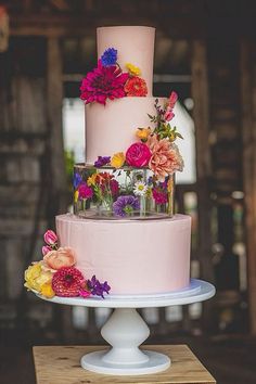 a three tiered cake with pink frosting and colorful flowers