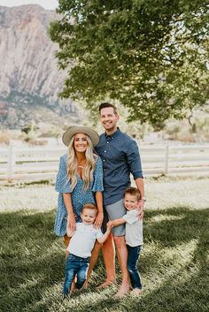 a family poses for a photo in front of a fence and tree with mountains in the background