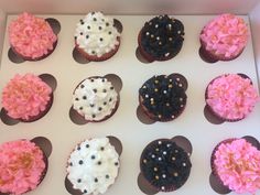 twelve cupcakes with pink and black frosting in a box