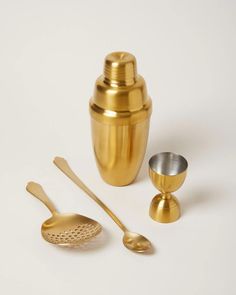 a set of golden kitchen utensils on a white surface with one spoon and two cups