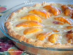 a close up of a pie with peaches on top and welcome home sign in the background