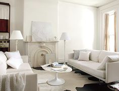 a living room filled with white furniture next to a fire place and two lamps on either side of the fireplace