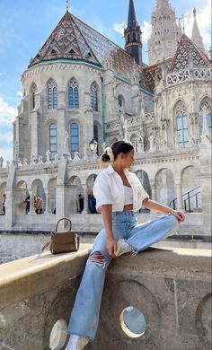 a woman sitting on top of a stone wall next to a large building with a clock tower