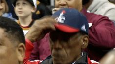 a baseball player adjusts his hat in front of other players at a game,